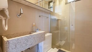A modern bathroom with a granite countertop, a glass shower enclosure, and a visible hairdryer. - Studio Moderno prox. do Shoppping Iguatemi SHL0105 (Lago Norte)