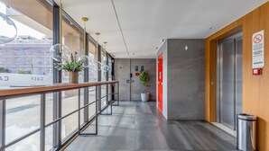A modern hallway with glass railings, potted plants, and a red elevator door. - ENE - Apartments in Noroeste in Brasilia (Brasília)