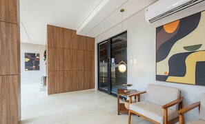 A modern interior with a wooden partition, a glass door leading to a parking area, and a large abstract painting on the wall. - EPK - Apartments in a Condo With Pool in Brasilia (Guará)