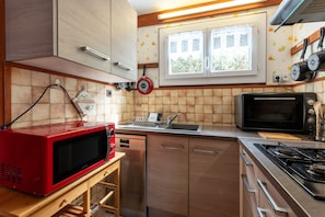 A kitchen with a red microwave, stainless steel appliances, a window with a view, and a tiled backsplash.