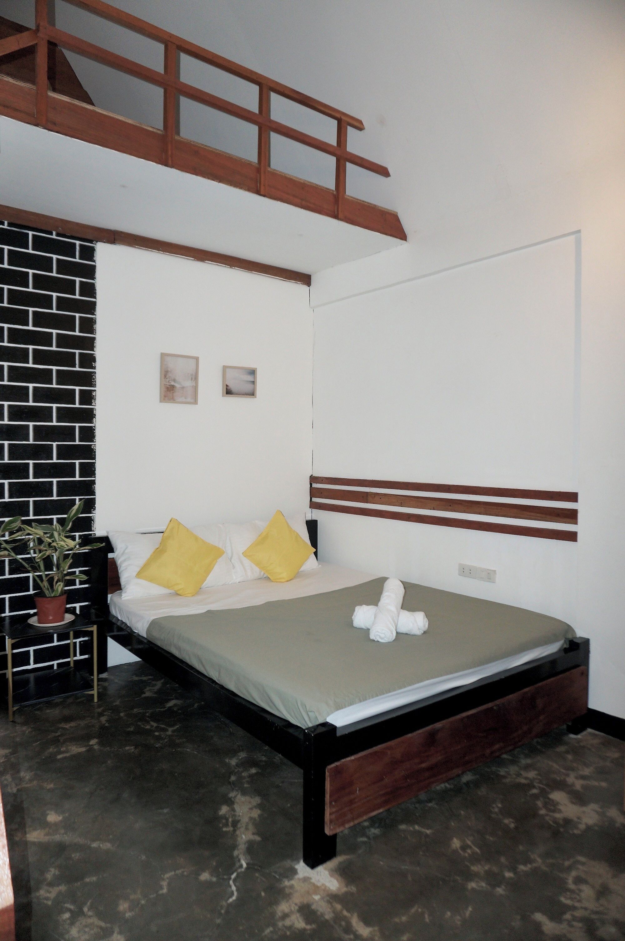 A bedroom with a bed, a wooden headboard, a brick wall, and a small potted plant.