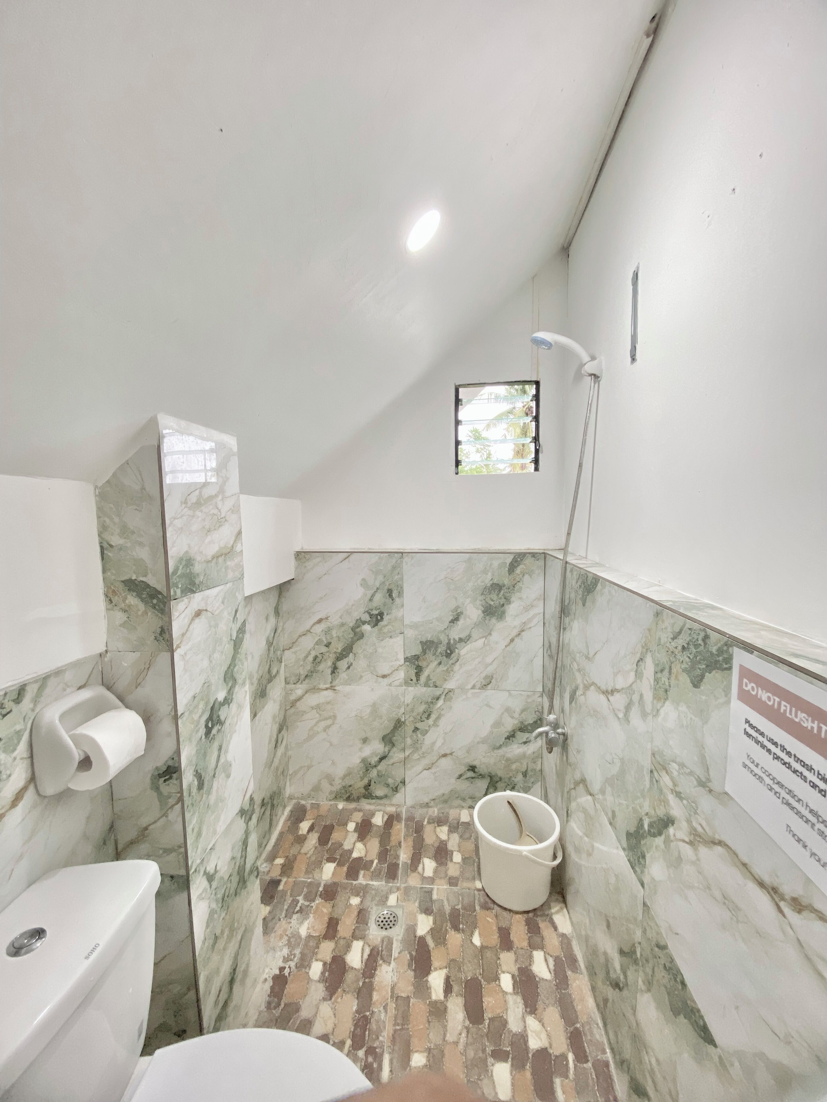 Baño con ducha, inodoro y pared con azulejos de mármol.