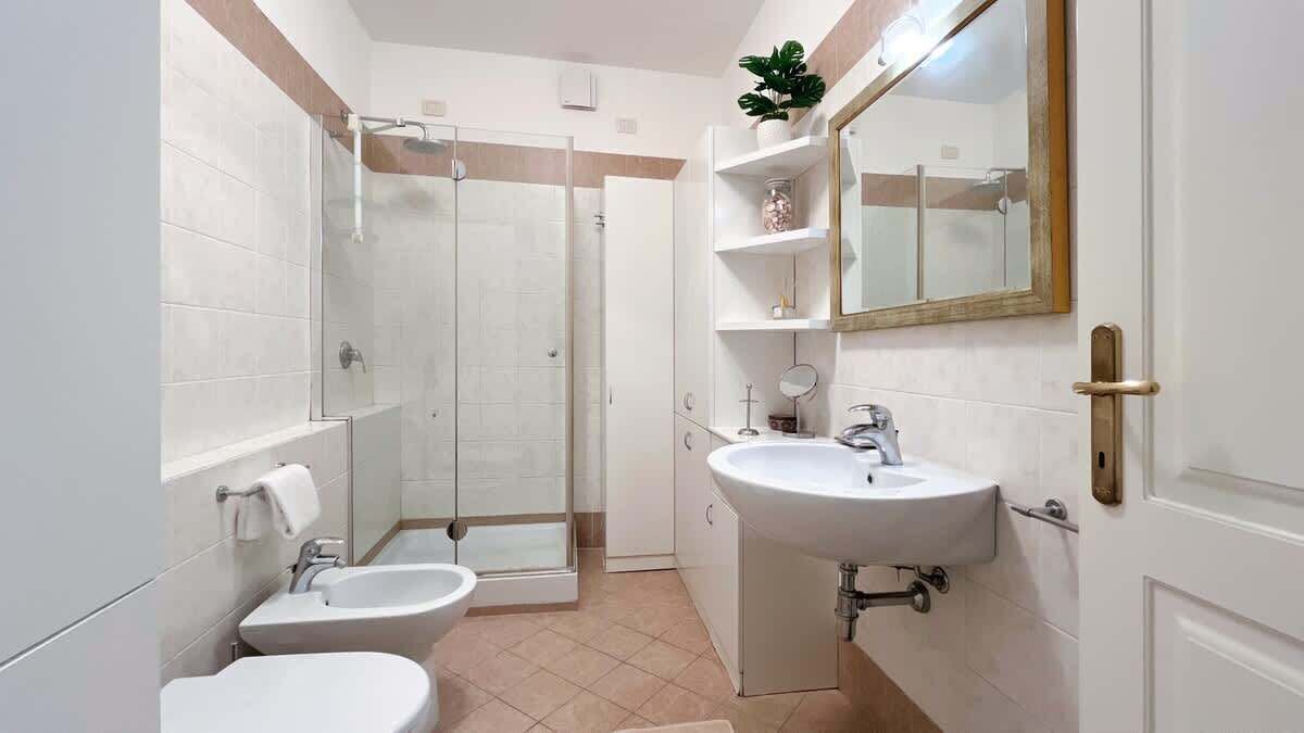 A bathroom with a shower, two sinks, a toilet, and a mirror.