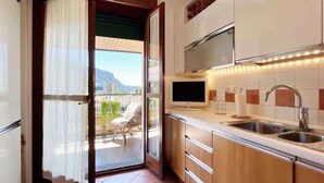 A modern kitchen with a large window, a flat-screen TV, and a balcony with a view of the mountains.