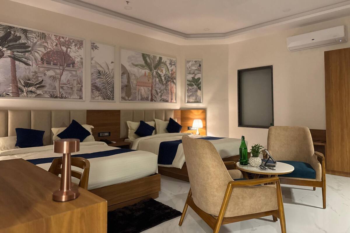 A hotel room with two beds, a desk, a chair, and a table with a bottle and a plant.