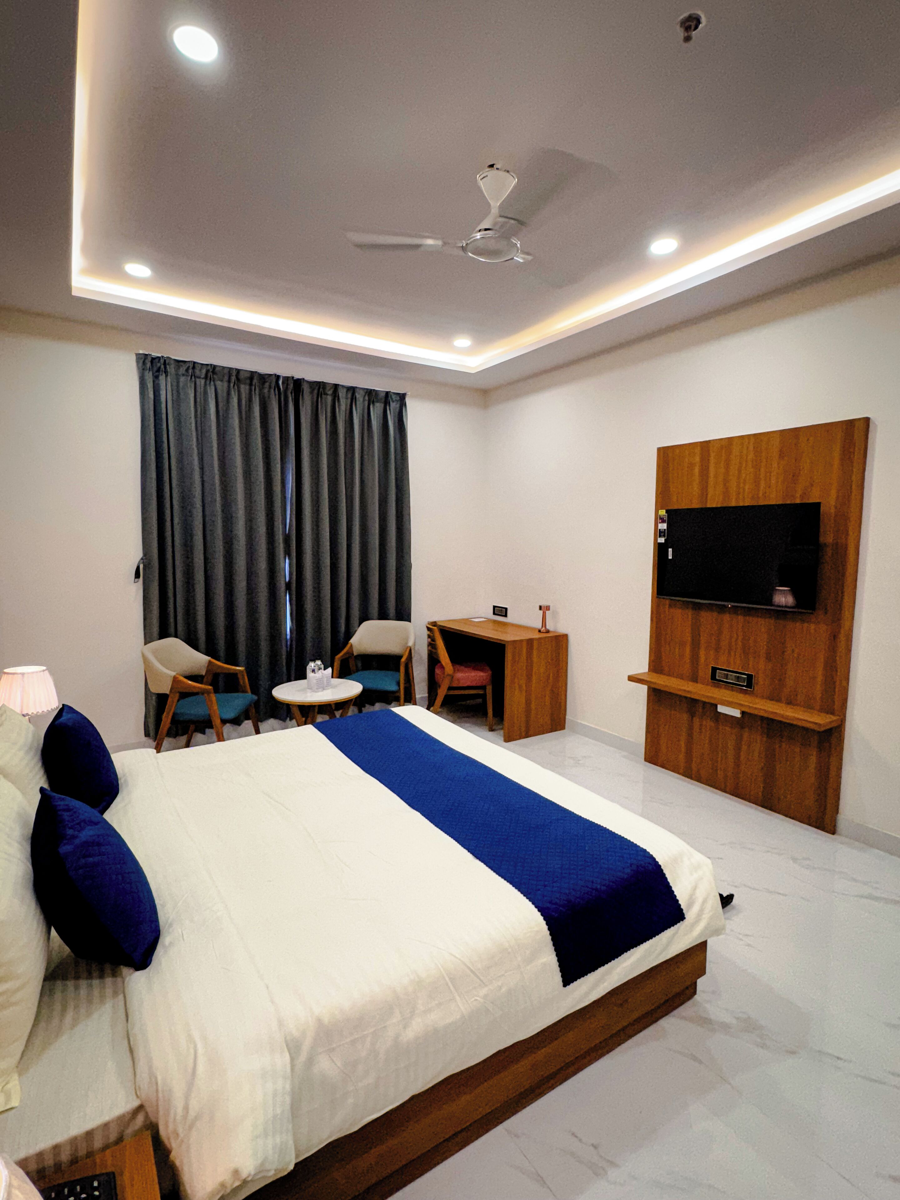A hotel room with a bed, a desk, a chair, a television, and a ceiling fan.