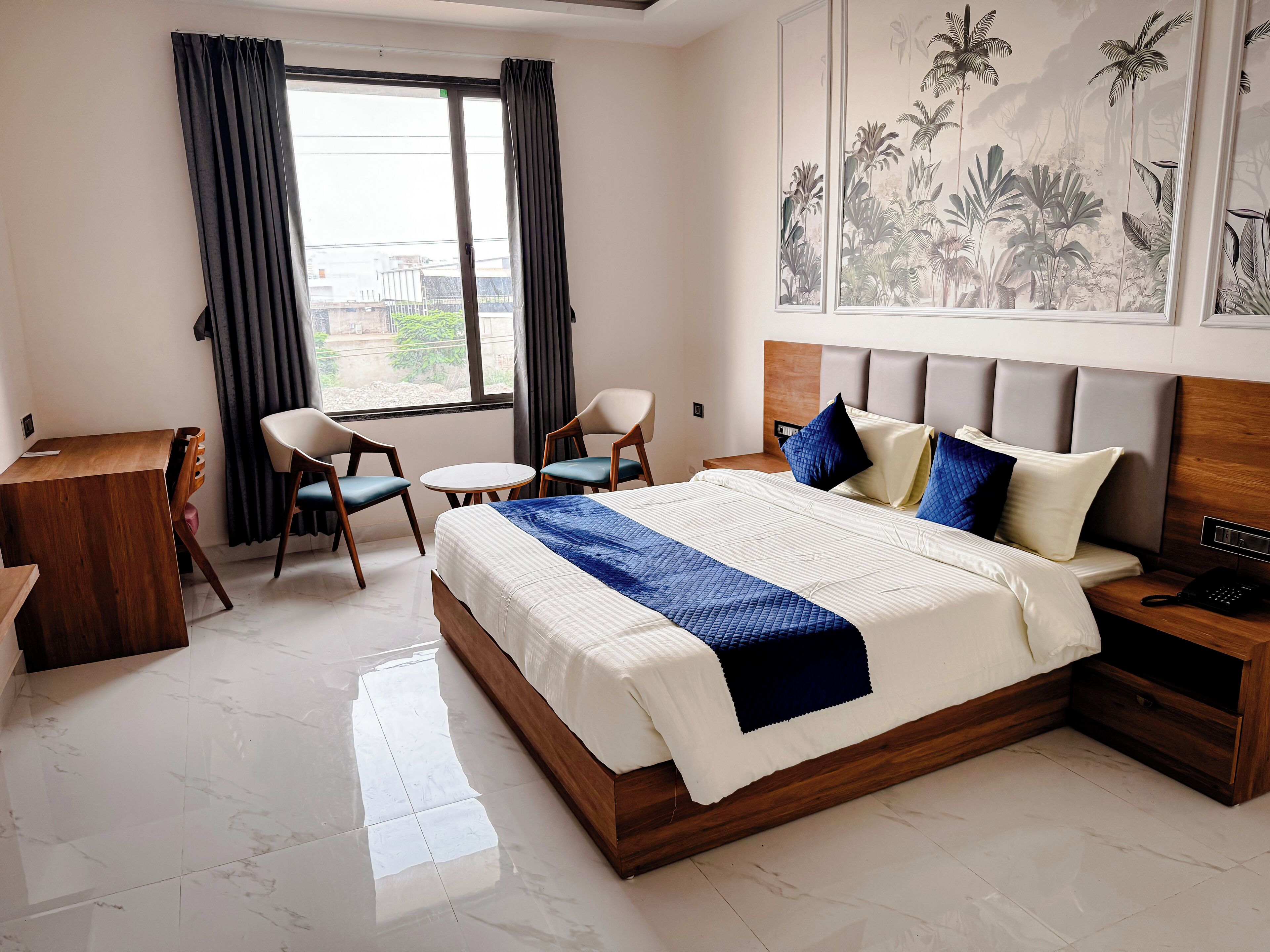 A hotel room with a bed, a desk, two chairs, a small table, and a nightstand.