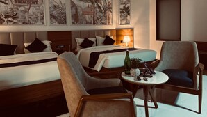 A hotel room with two beds, a sitting area with a table, and artwork on the walls. - Hotel Blue Ocean (Udaipur)