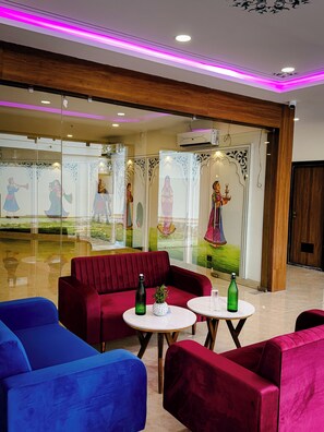 A hotel lobby with red and blue seating, decorative glass panels, and a ceiling with pink lighting. - Hotel Blue Ocean (Udaipur)