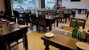 A restaurant with multiple tables, chairs, and a large window offering a view of the street. - Hotel Blue Ocean (Udaipur)