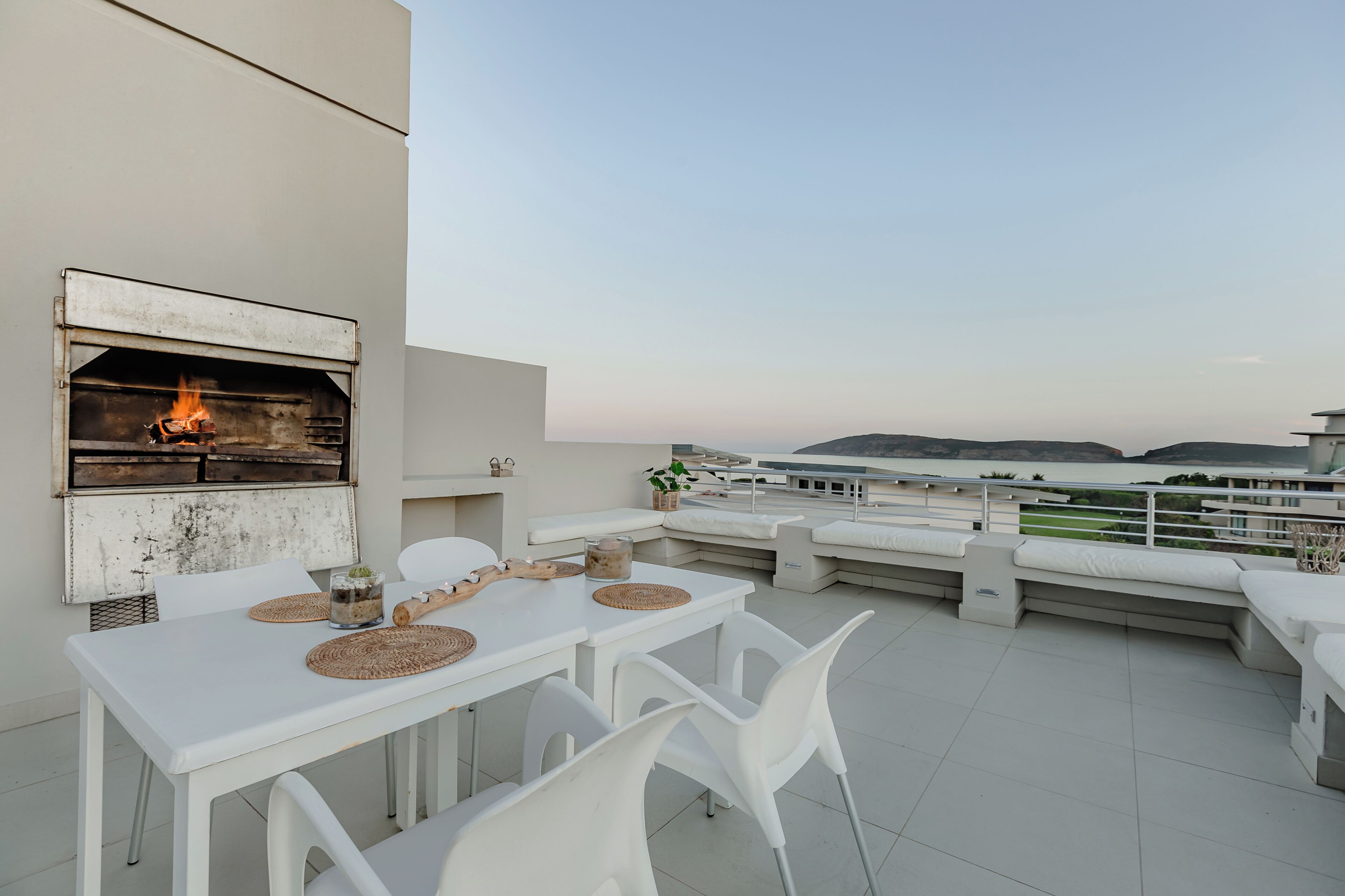 A rooftop terrace with a built-in grill, white furniture, and a view of the sea.