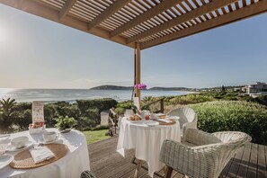 A deck with a table set for breakfast overlooking a scenic ocean view. - Cottage Pie by Robberg (Plettenberg Bay)