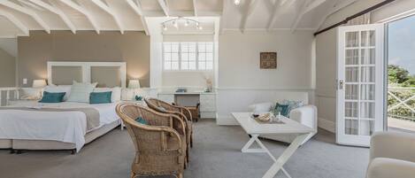 A spacious bedroom with a large bed, a desk, wicker chairs, and a balcony with a view.