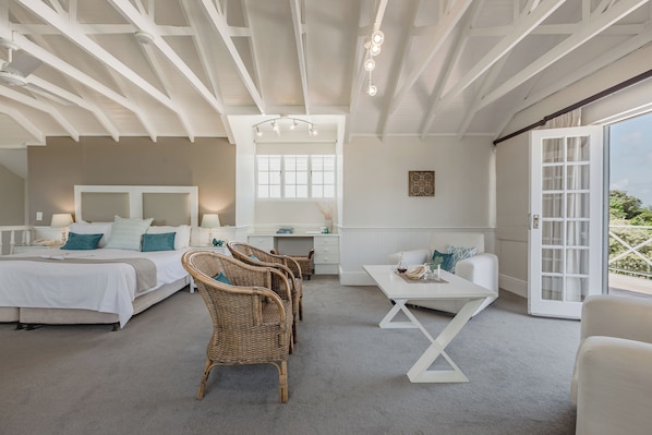 A spacious bedroom with a large bed, a desk, wicker chairs, and a balcony with a view. - Cottage Pie by Robberg (Plettenberg Bay)