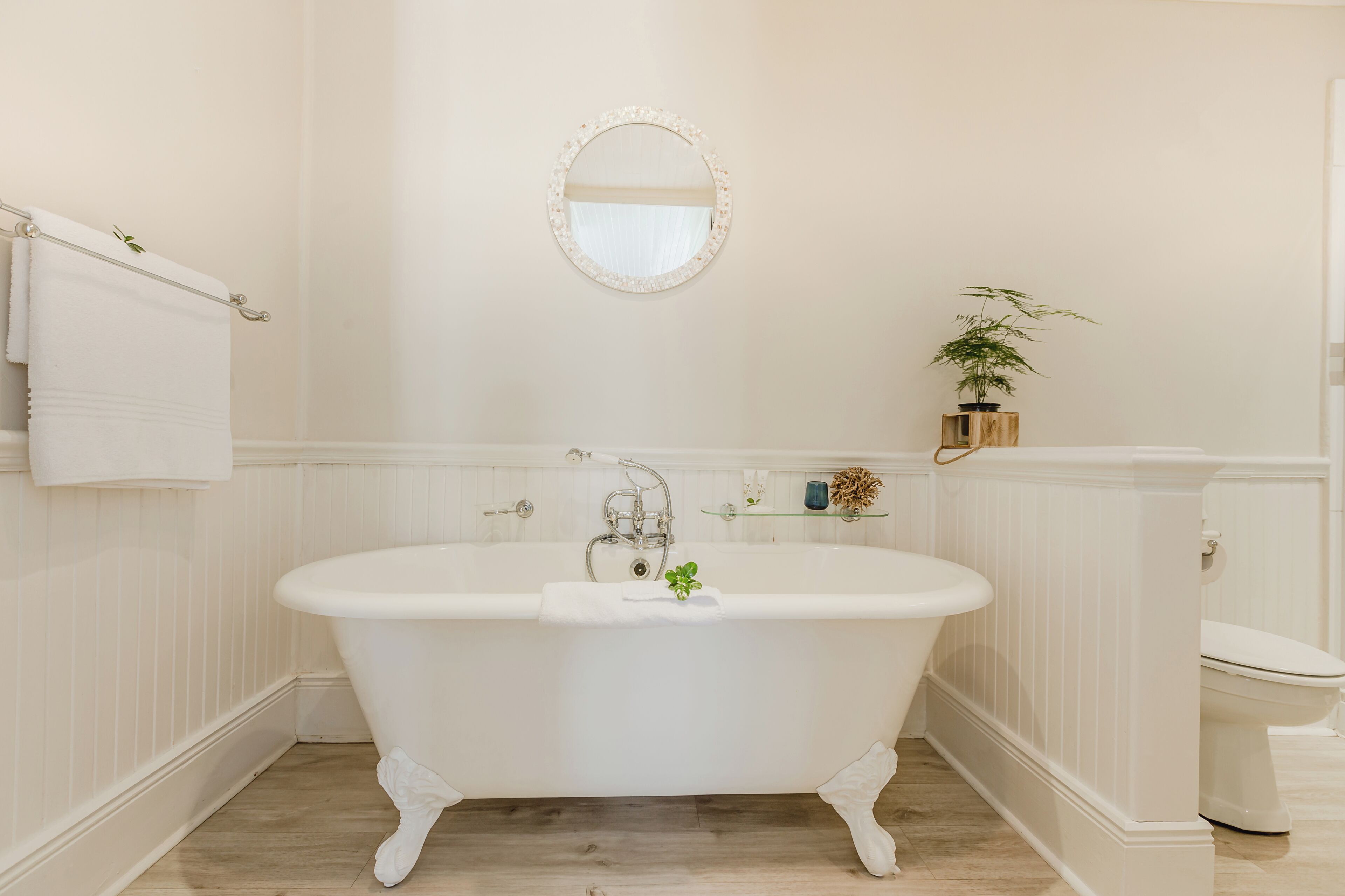 A bathroom with a freestanding bathtub, a toilet, a mirror, and a plant.