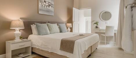 A bedroom with a bed, nightstand, desk, chair, and a mirror.