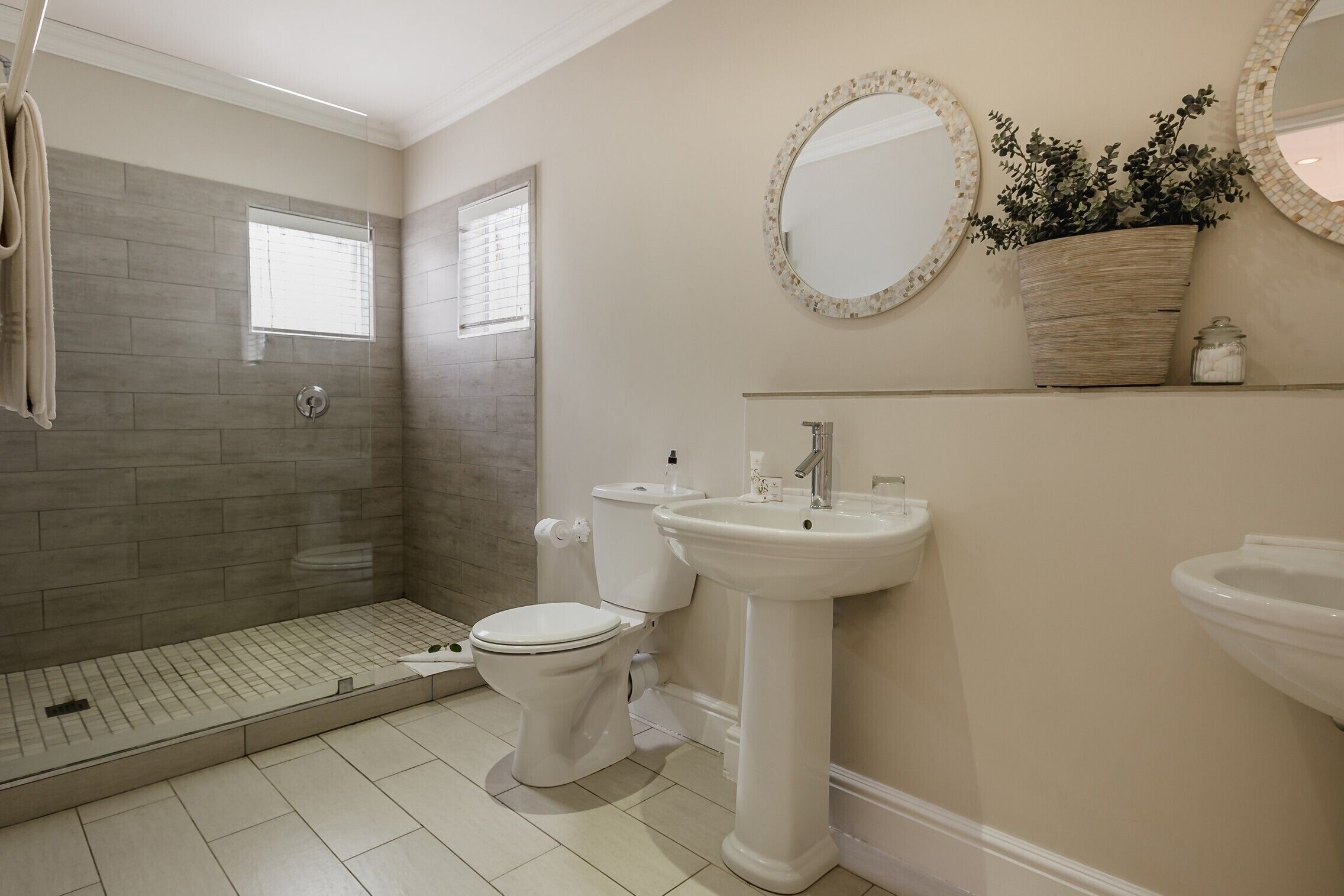A bathroom with a shower, toilet, sink, and two mirrors.