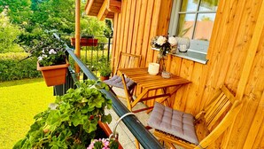 Eine Holzdiele mit Balkon, Sitzgelegenheit im Freien und Blumentöpfen.