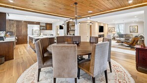 Uma cozinha moderna com armários de madeira, uma sala de jantar com mesa e cadeiras redondas, e uma sala de estar com sofá e mesinha de centro.