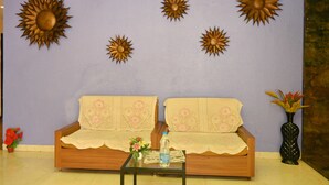 A living room with a sofa, a coffee table, and decorative sun-shaped wall art. - Hotel Ryaan Inn  (Raipur)
