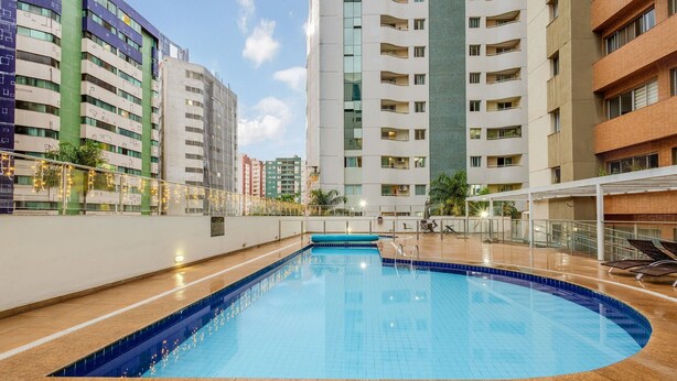 A swimming pool with a blue tiled edge, surrounded by a low brick wall and a glass railing. - Luxury Penthouse w/ Jacuzzi in Brasilia Bcy2001 (Águas Claras)
