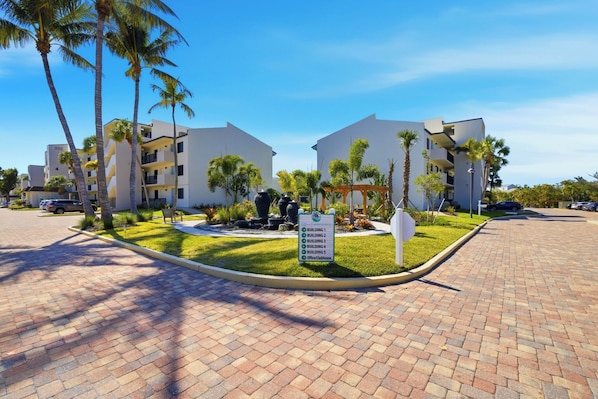 A modern hotel complex with a landscaped courtyard, palm trees, and a sign indicating building numbers and the office location.