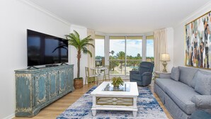 A living room with a television, a sofa, a coffee table, and a view of the outdoors.
