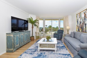 A living room with a television, a sofa, a coffee table, and a view of the outdoors. - Silver Shells St. Croix 302 by Compass Resorts (Destin)
