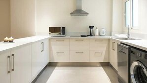 A modern kitchen with white cabinets, a stainless steel range hood, a built-in oven, and a dishwasher. - Kennah Milena | Akoya Residence, New Cairo (New Cairo)