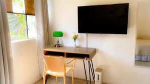 Een kleine kamer met een bureau, stoel, televisie en een raam met gordijnen.