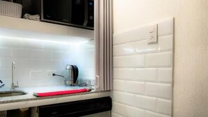 A kitchen with white tiled walls, a black dishwasher, a red cutting board, and a coffee maker.