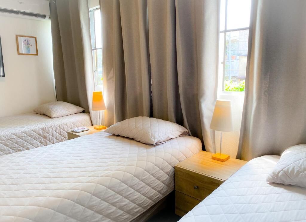 Ett hotellrum med två sängar, var och en med ett vitt, vadderat sängöverkast och matchande kuddar. Det finns två sängbord med lampor, och rummet har ett stort fönster med gardiner.