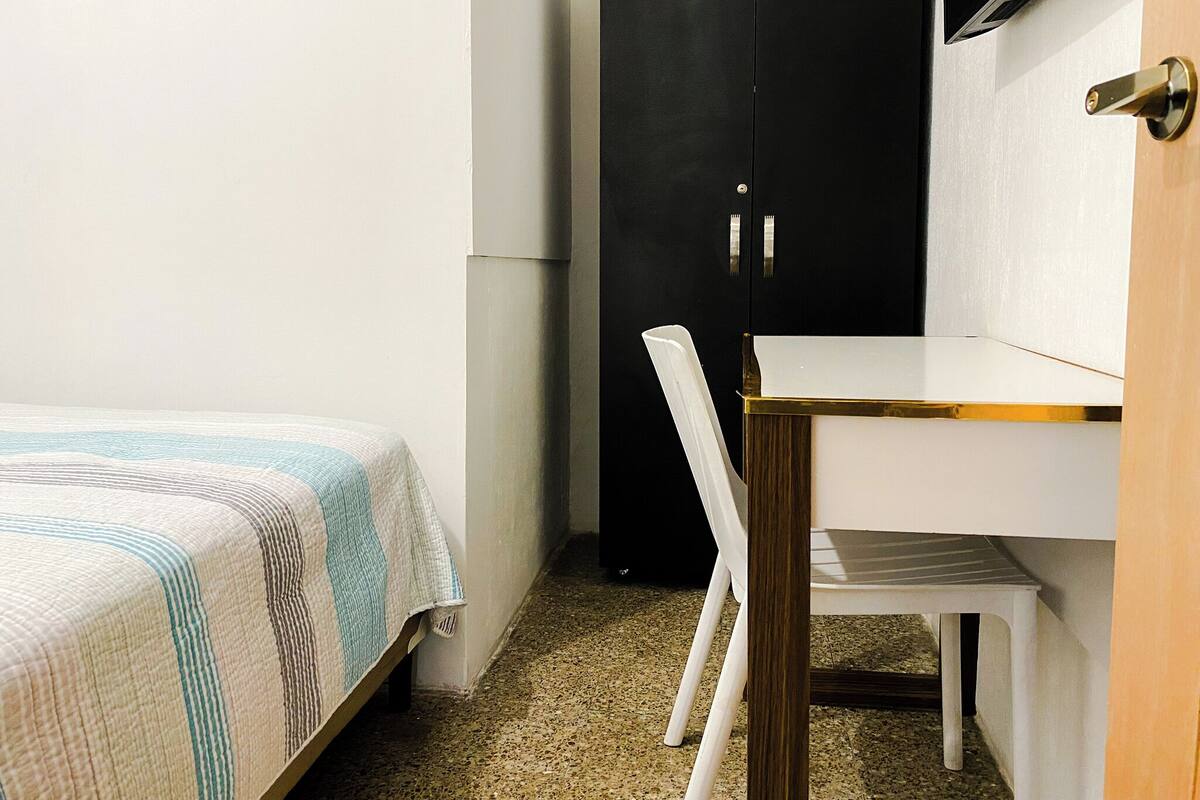 Een kleine, verzorgde slaapkamer met een bed, een bureau en een stoel.