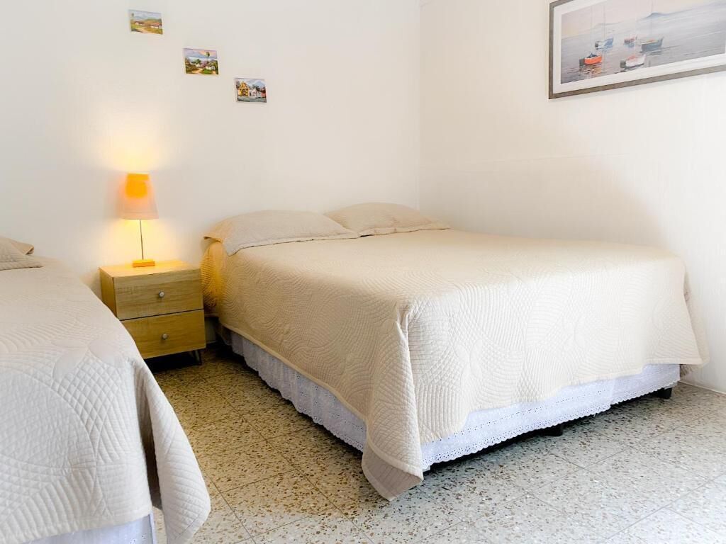 A bedroom with a bed, a bedside table with a lamp, and a small drawer.