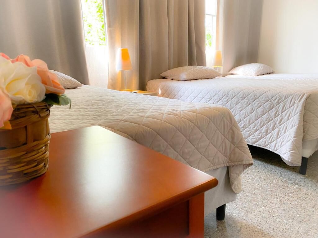 Une chambre d’hôtel avec deux lits, une table de chevet en bois et un panier en osier rempli de fleurs.