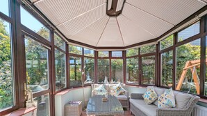 Une véranda avec de grandes fenêtres, des meubles en osier et un sol carrelé.