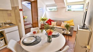 A compact living space with a dining area, kitchenette, and a sofa with cushions.