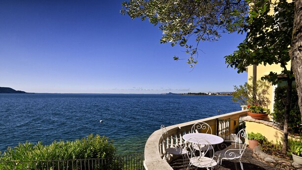 A terrace with a view of the sea, outdoor seating, and potted plants.
