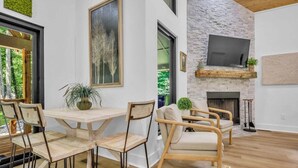 A modern living room with a stone wall, a fireplace, and a large TV mounted above it. There are wooden chairs and a table with chairs. - Forest Haven 1030-Luxe Cabin-Sleeps 7 (Kingston Springs)