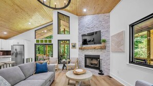 A modern living room with a grey sofa, a round wooden coffee table, and a stone fireplace. - Forest Haven 1030-Luxe Cabin-Sleeps 7 (Kingston Springs)