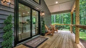 A wooden deck with a welcome mat, a glass door, and a view of the surrounding greenery. - Forest Haven 1030-Luxe Cabin-Sleeps 7 (Kingston Springs)