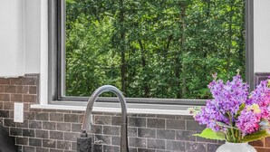 A kitchen with a double sink, a modern faucet, a pendant light, and a window with a view of a forest. - Forest Haven 1030-Luxe Cabin-Sleeps 7 (Kingston Springs)