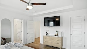 A bedroom with a bed, a ceiling fan, a TV mounted on the wall, a dresser, and white doors. - New modern Townhouse, 3BR, 2.5B, near Mid City (Huntsville)