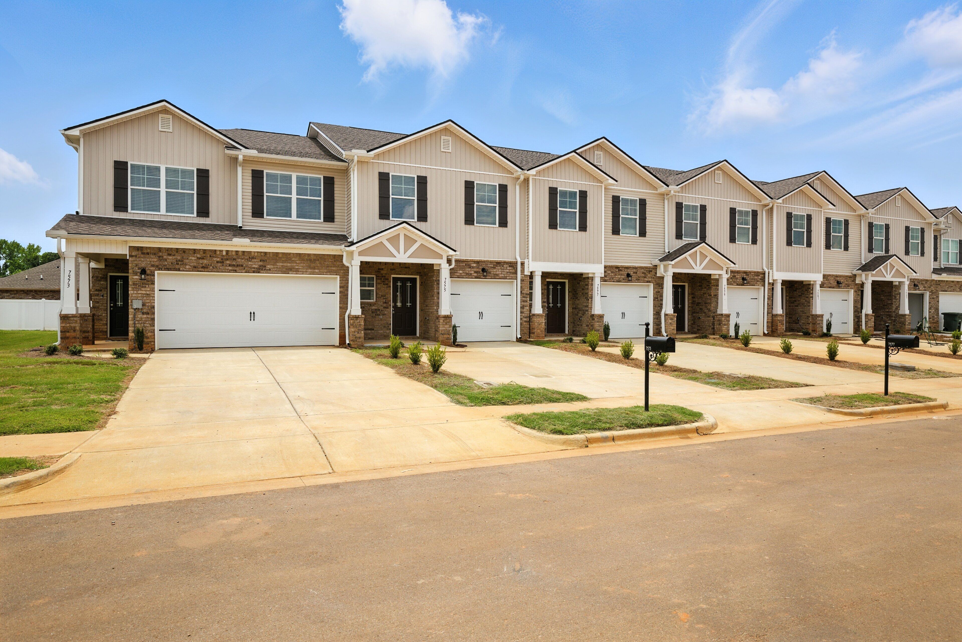 A row of townhouses with attached garages, a front lawn, and a clear sky.