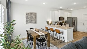 A modern kitchen with white cabinets, a central island with bar stools, and a dining area with a wooden table and chairs. - New modern Townhouse, 3BR, 2.5B, near Mid City (Huntsville)