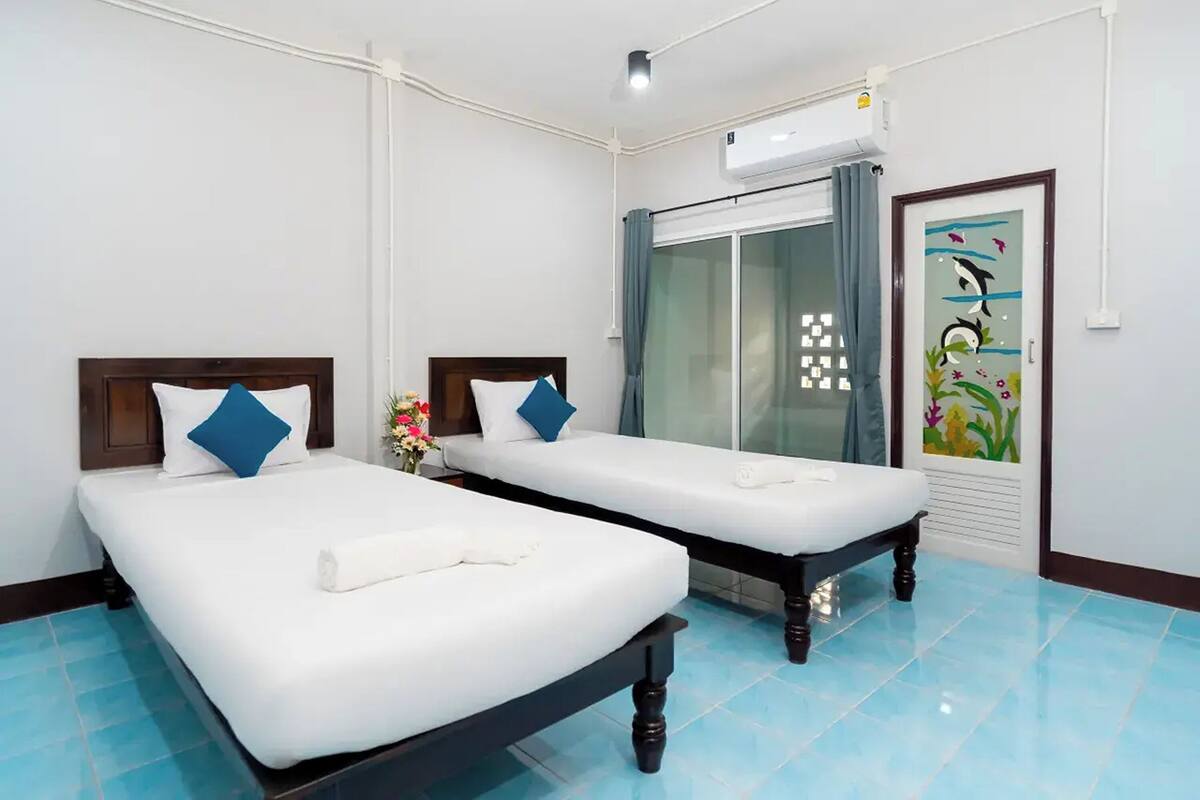 Ein Hotelzimmer mit zwei Betten, einem großen Fenster mit Vorhängen, einer Klimaanlage und einem dekorativen Wandgemälde mit Fischmotiven.
