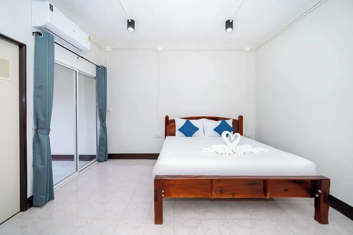 Ein Schlafzimmer mit einem hölzernen Bett, weißer Bettwäsche und einem großen Fenster mit Vorhängen.