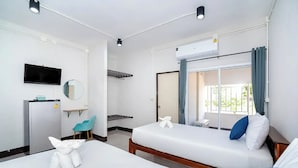 Habitación de hotel con dos camas, televisión, espejo, refrigerador, una mesita y ventana con cortinas.