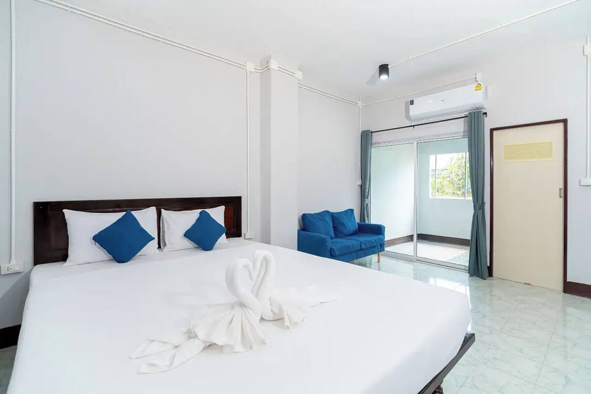 Ein Hotelzimmer mit einem großen Bett, einem blauen Sofa, einer Schiebetür aus Glas und einer Klimaanlage.