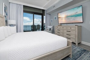 A hotel room with a large bed, a dresser, a TV, and a balcony with a view of the ocean. - Phoenix Gulf Shores Ii 1002 3 Bedroom Condo (Gulf Shores)